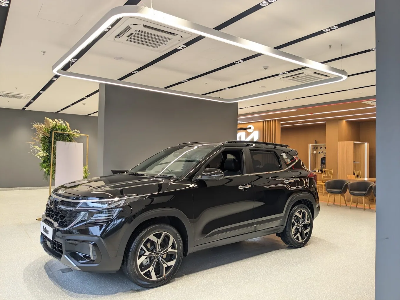 Spacious car showroom floor featuring glossy white tiled flooring, black structural columns, and large overhead lightboxes displaying new vehicles.